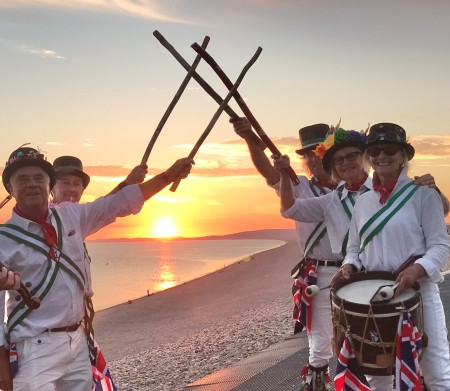 Lyme Morris group with sticks in the air and the sunrise behind them, rising over the beach